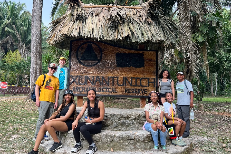 students and faculty stand together by a wooden sign