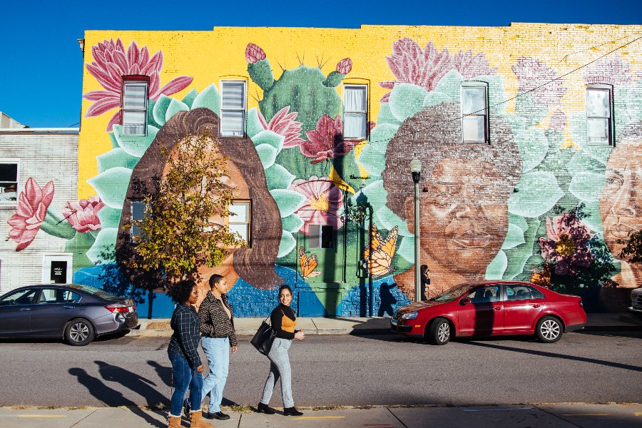 three students walk in front of a brightly colored mural